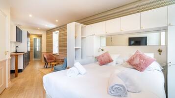 Una moderna camera d'albergo con un letto grande, un'area salotto con una poltrona, una piccola scrivania e un bagno visibile attraverso una porta aperta.
