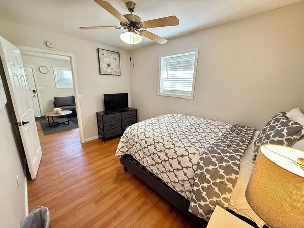 Un dormitorio con cama, ventilador de techo, televisión, cómoda, ventana y puerta.
