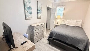 A bedroom with a bed, a desk with a computer, a dresser, and artwork on the wall.