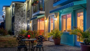 A building with a stone facade, a balcony with potted plants, and a patio area with a table and chairs.