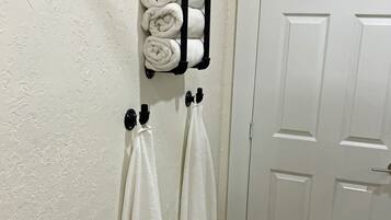 Un baño con una puerta blanca, un perchero con toallas enrolladas y dos toallas colgadas de ganchos.