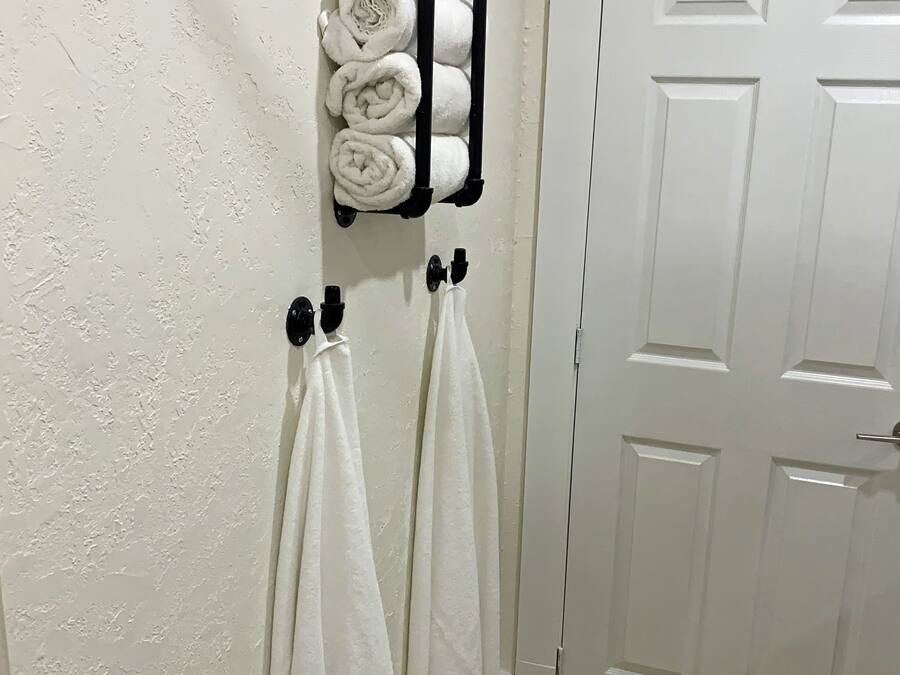Un baño con una puerta blanca, un perchero con toallas enrolladas y dos toallas colgadas de ganchos.
