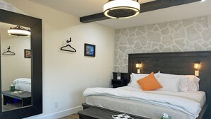 A hotel room with a bed, a bench, a mirror, a nightstand, and a wall-mounted light fixture.