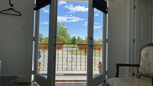 An open sliding glass door leading to a balcony with a view of a garden and a clear sky.