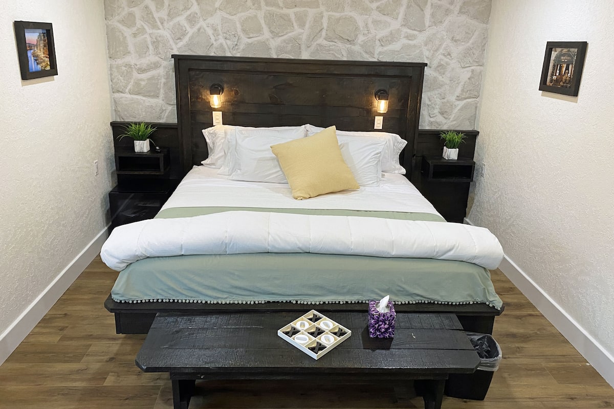 Un dormitorio ordenado con pared de piedra, cabecera de madera y mesitas de noche con plantas.