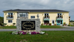 A two-story boutique hotel with a stone sign, balconies with potted plants, and a well-maintained lawn.