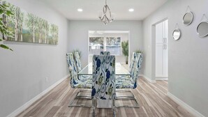 A dining area with a glass-top table, chairs with floral upholstery, a chandelier, and a view through a window. - Spacious House w/ Patio & Fenced Yard (Lakeland)