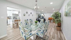 A modern dining area with a glass table, floral-patterned chairs, a chandelier, and a potted plant. - Spacious House w/ Patio & Fenced Yard (Lakeland)