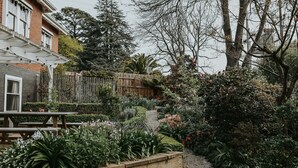 A garden with a wooden bench, a pathway, and a variety of plants and flowers. - Vagabond's Rest & Rose Gold Hideaway - A Colourful 5-Bedroom in East Launceston (East Launceston)