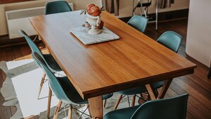 A wooden dining table with four green chairs, a white marble placemat, and a decorative fruit centerpiece. - Vagabond's Rest & Rose Gold Hideaway - A Colourful 5-Bedroom in East Launceston (East Launceston)