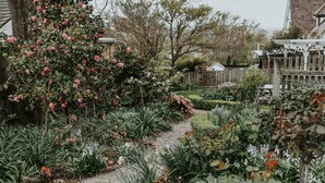 A garden with a variety of plants and flowers, a gravel path, and a wooden fence. - Vagabond's Rest & Rose Gold Hideaway - A Colourful 5-Bedroom in East Launceston (East Launceston)