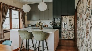 A modern kitchen with a central island, bar stools, and a refrigerator with floral wallpaper. - Vagabond's Rest & Rose Gold Hideaway - A Colourful 5-Bedroom in East Launceston (East Launceston)