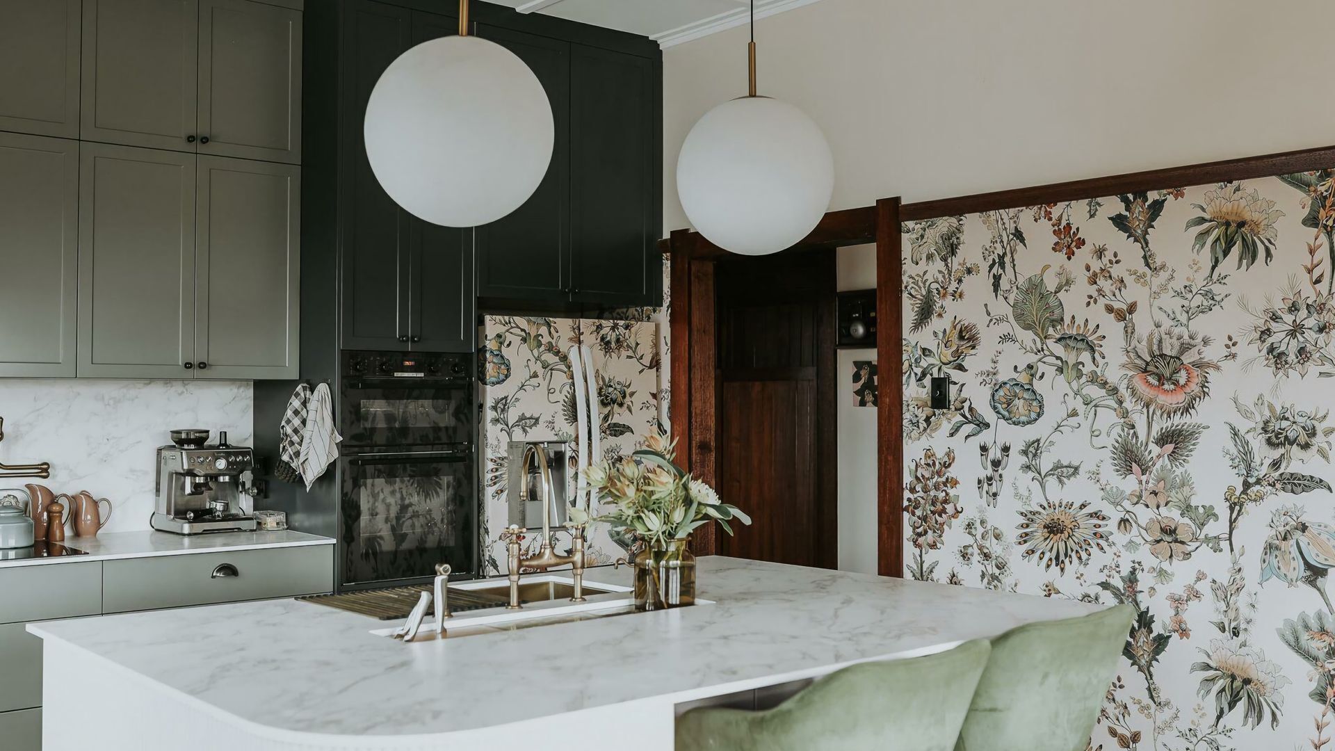 A kitchen with dark cabinets, a marble countertop, a coffee machine, and a floral wallpaper.