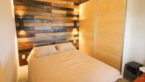 A bedroom with a bed, wooden headboard, bedside lamps, and a wardrobe. - Sunset Ranch, a private acre lot facing open ranch land and high planes desert (Marathon)