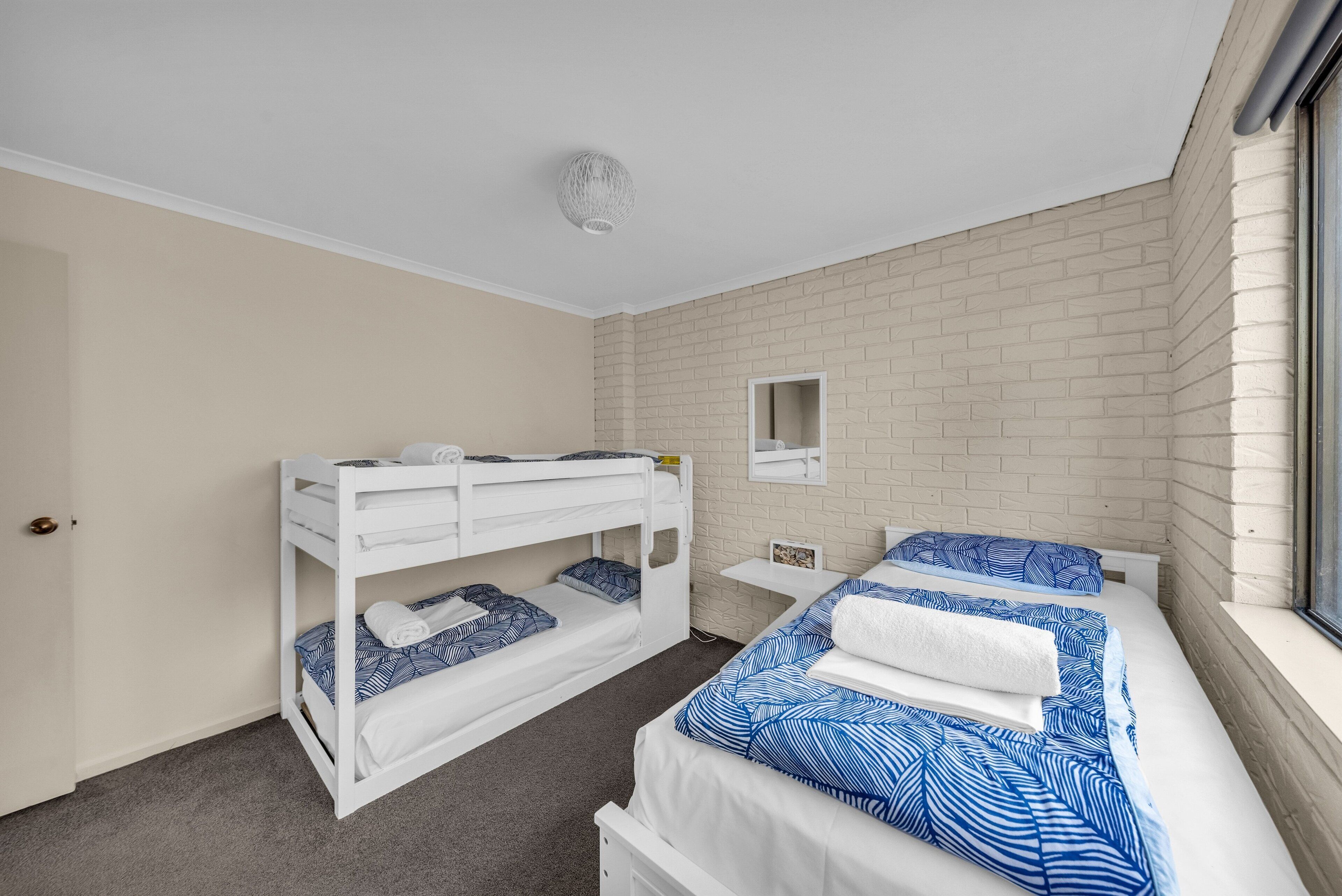 A room with two bunk beds, a small bedside table, a mirror, and a window.