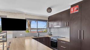 A modern kitchen with a large window, dark cabinets, and a flat-screen TV.