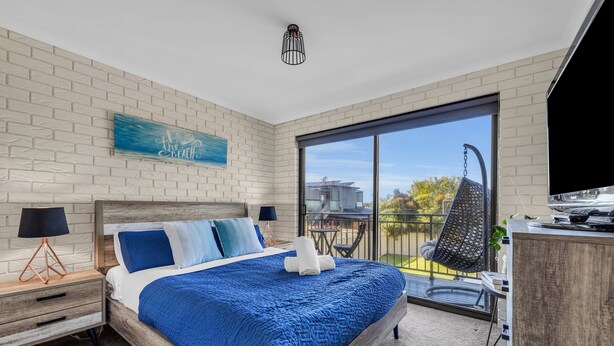 A modern bedroom with a large bed, a TV, and a balcony with outdoor furniture.