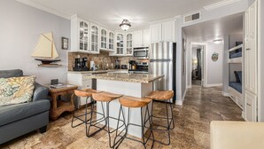 A modern kitchen with white cabinets, a stainless steel refrigerator, and a central island with bar stools. - Condo w/Beach/Pool Views Over-sized Balcony - w/d in unit & bidet (Galveston)