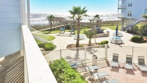 A hotel courtyard with outdoor seating, palm trees, and a view of the ocean. - Condo w/Beach/Pool Views Over-sized Balcony - w/d in unit & bidet (Galveston)
