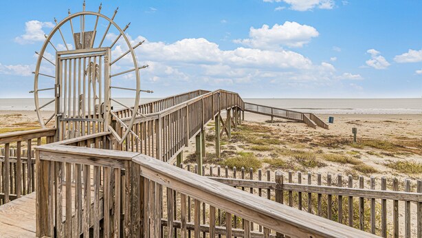 A wooden boardwalk leading to a large wheel structure on a beach. - Condo w/Beach/Pool Views Over-sized Balcony - w/d in unit & bidet (Galveston)