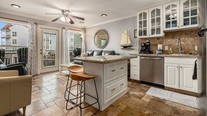 A spacious kitchen with white cabinetry, a central island with stools, a ceiling fan, and a view to the outside. - Condo w/Beach/Pool Views Over-sized Balcony - w/d in unit & bidet (Galveston)