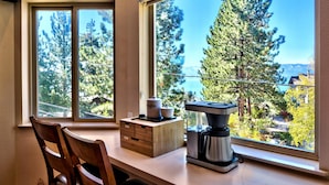 Une cuisine équipée d’une machine à café, de meubles en bois et offrant une vue sur les arbres et les montagnes grâce à de grandes fenêtres.