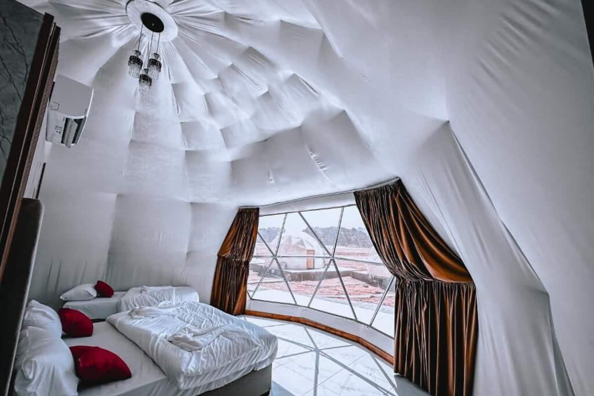 Una habitación con un techo geométrico singular, un ventanal con cortinas y una cama con almohadas.