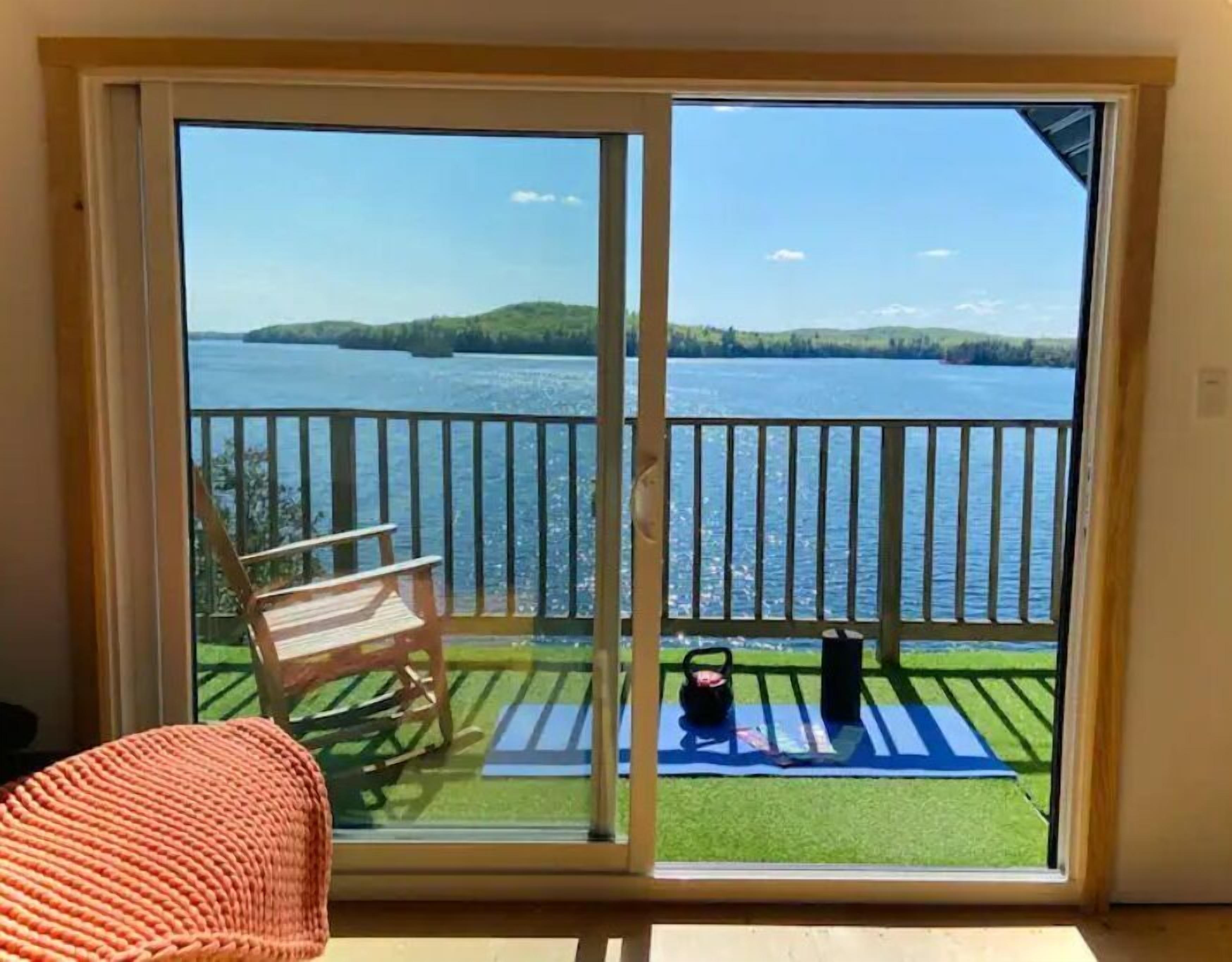 Une pièce dotée d’une porte-fenêtre coulissante donnant sur un balcon avec vue sur un lac et des collines.
