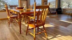Un espace repas avec une table et des chaises en bois, de grandes fenêtres et une vue sur l’extérieur.