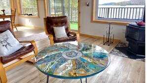 Une pièce chaleureuse avec une table en verre, des fauteuils en cuir, une cheminée et une vue sur un lac.