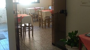 An interior view of a dining area with tables and chairs, a potted plant, and a window with a view. - Pousada Samambaia  (Sao Lourenco)