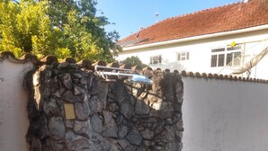 A stone wall with a blue-tiled circular area, a stone floor, and a white building with a red-tiled roof in the background. - Pousada Samambaia  (Sao Lourenco)