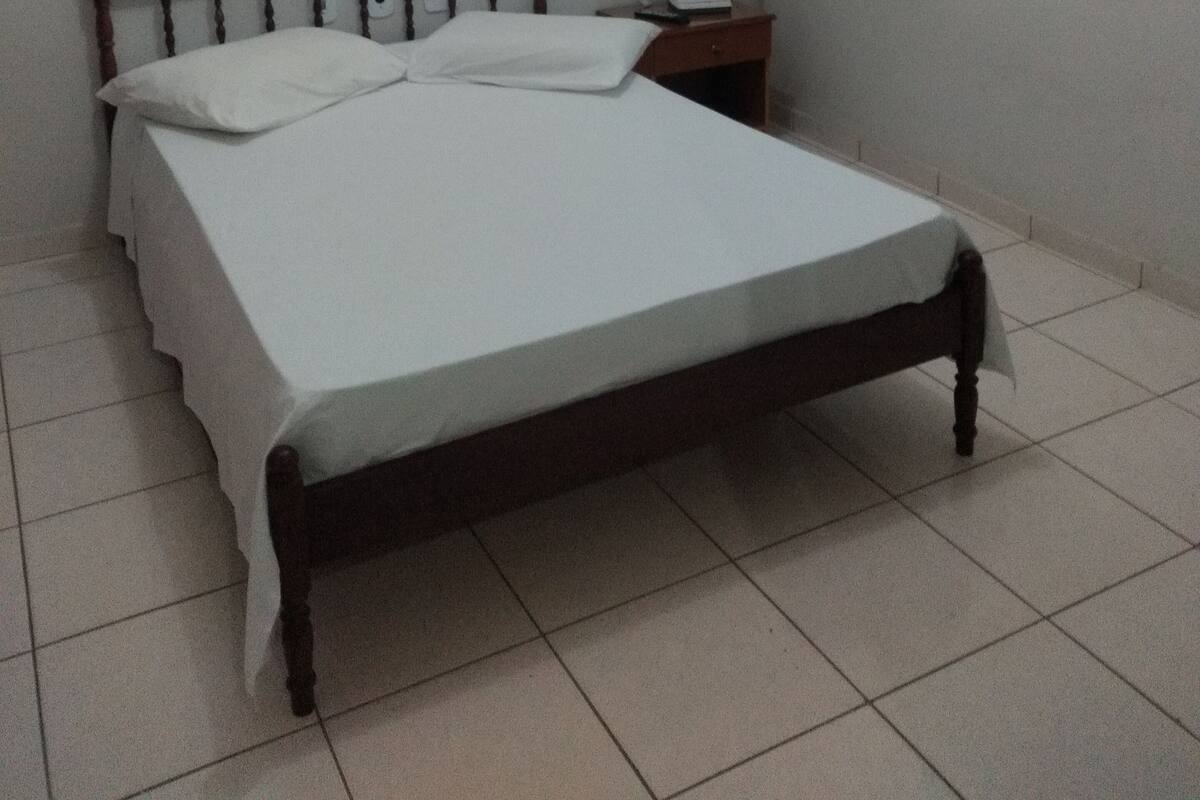 Habitación individual con una cama que tiene cabecera de madera, una mesita de noche con lámpara, y una lámpara fijada en la pared.