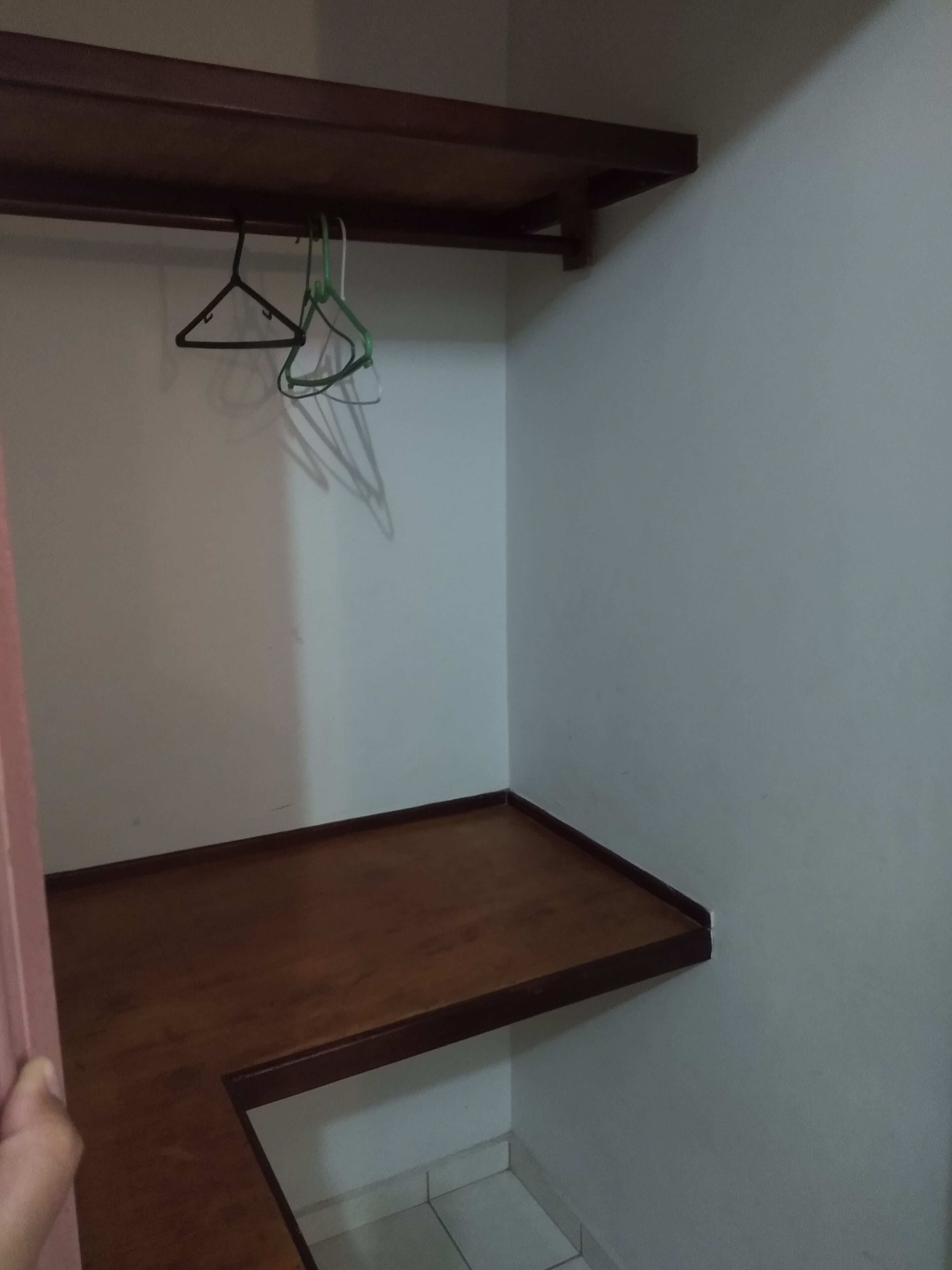 Een hoek van een kamer met een houten plank en een kledingrek.
