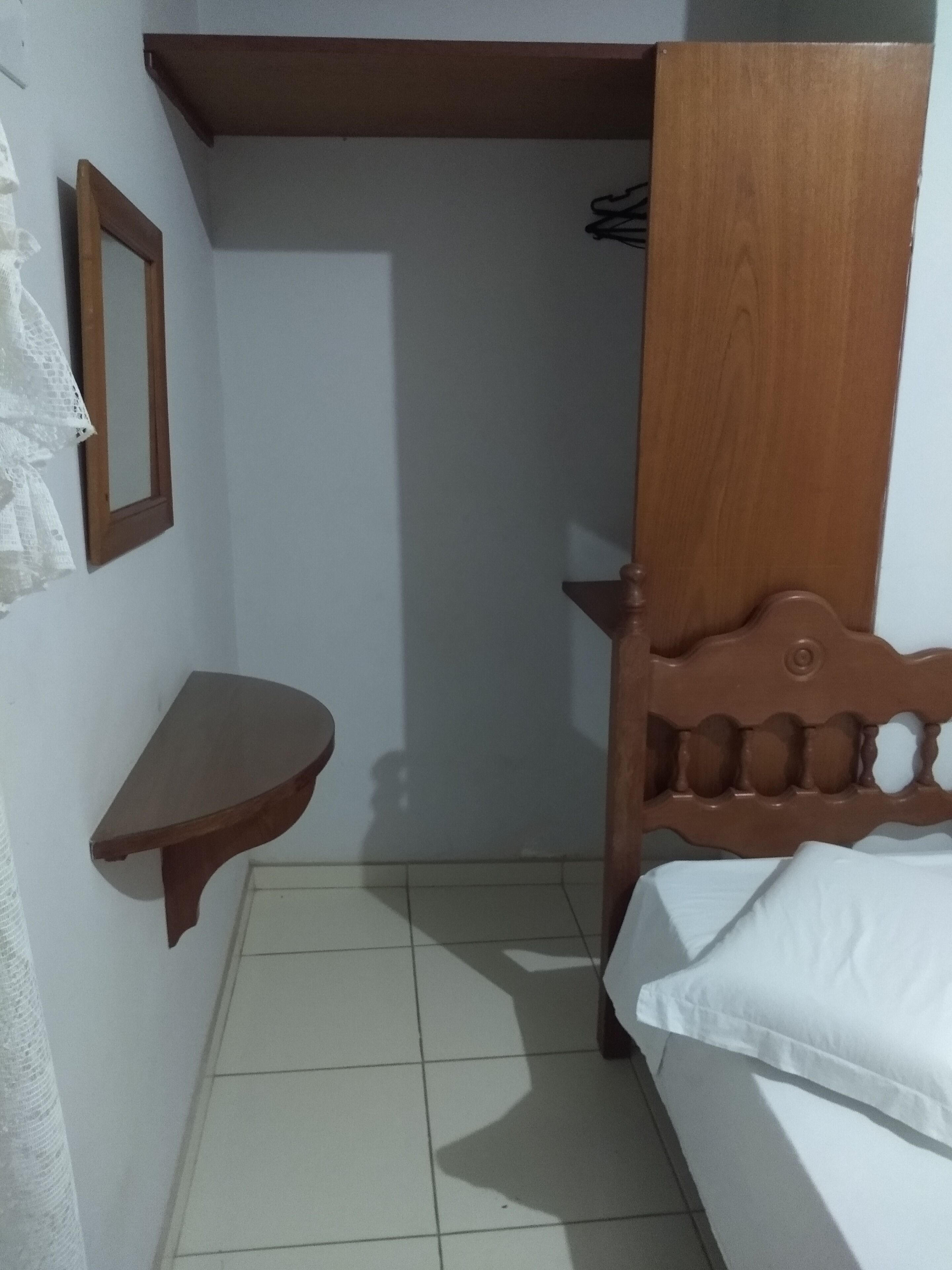 A small, narrow room with a wooden bed, a wooden shelf, and a mirror on the wall.