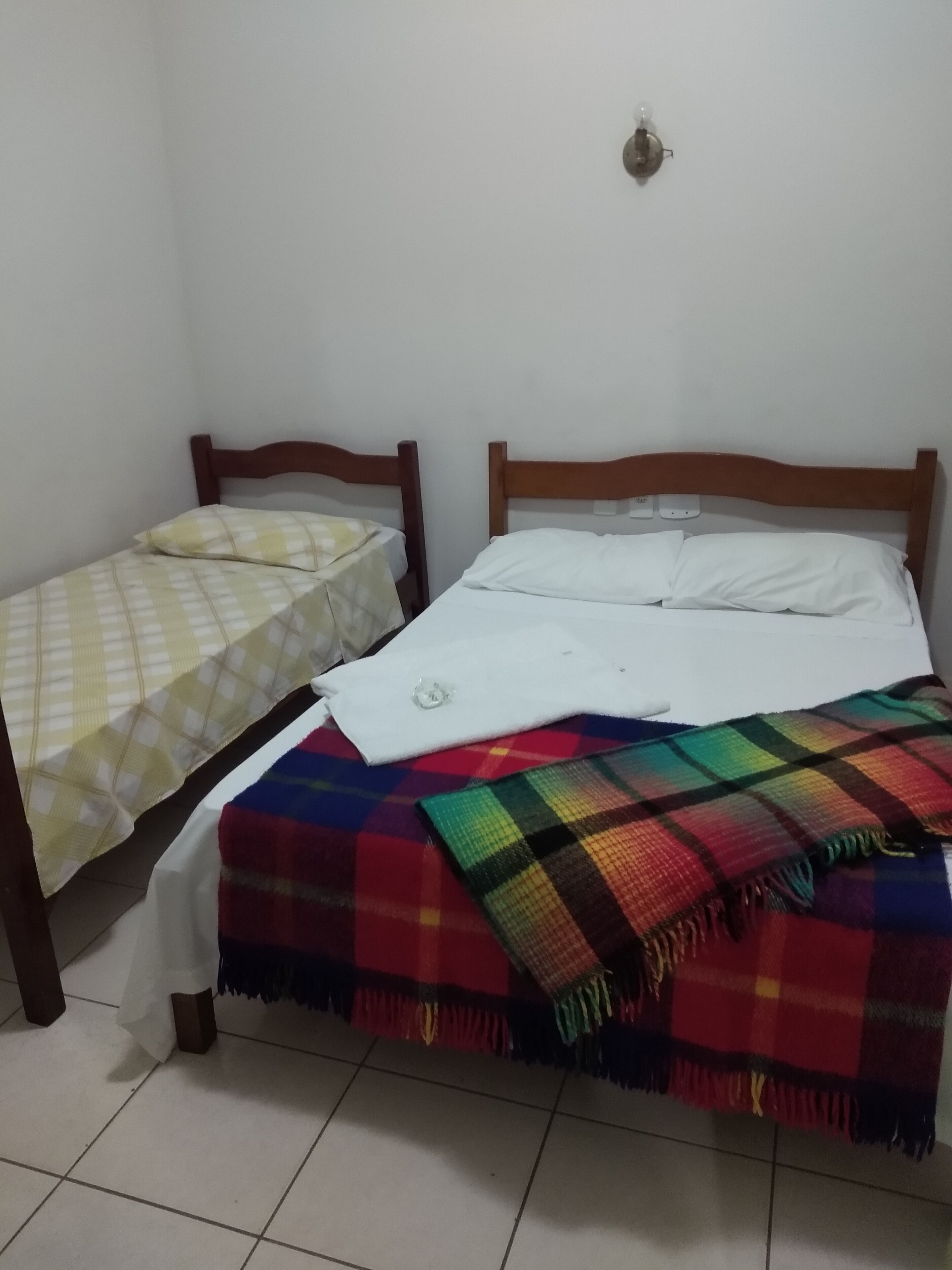 A room with two wooden beds, one with a checkered bedspread and the other with a white bedspread and a colorful blanket.