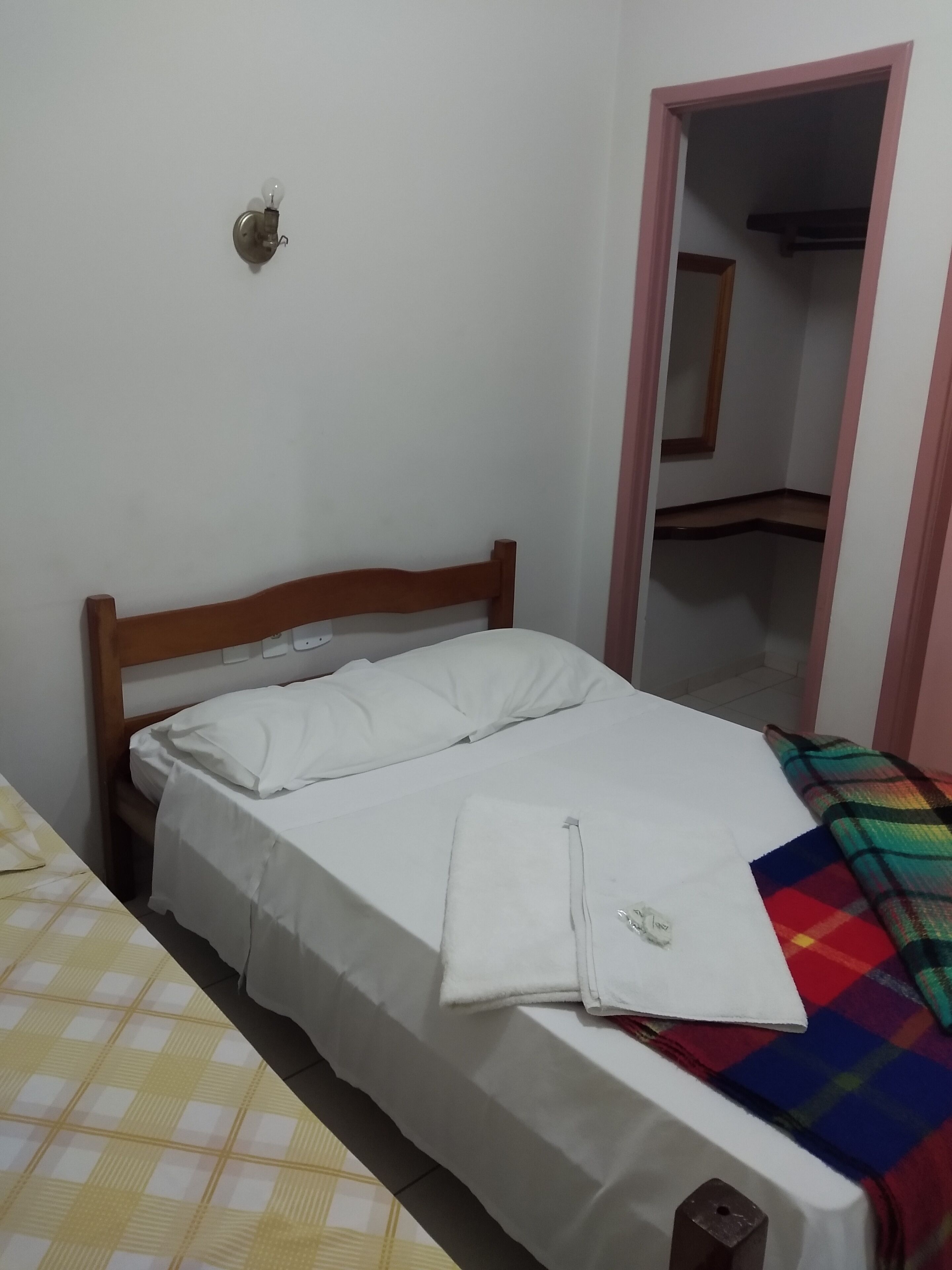 A single bed with a wooden headboard, a white pillow, and a colorful blanket. A small white object is on the bed.