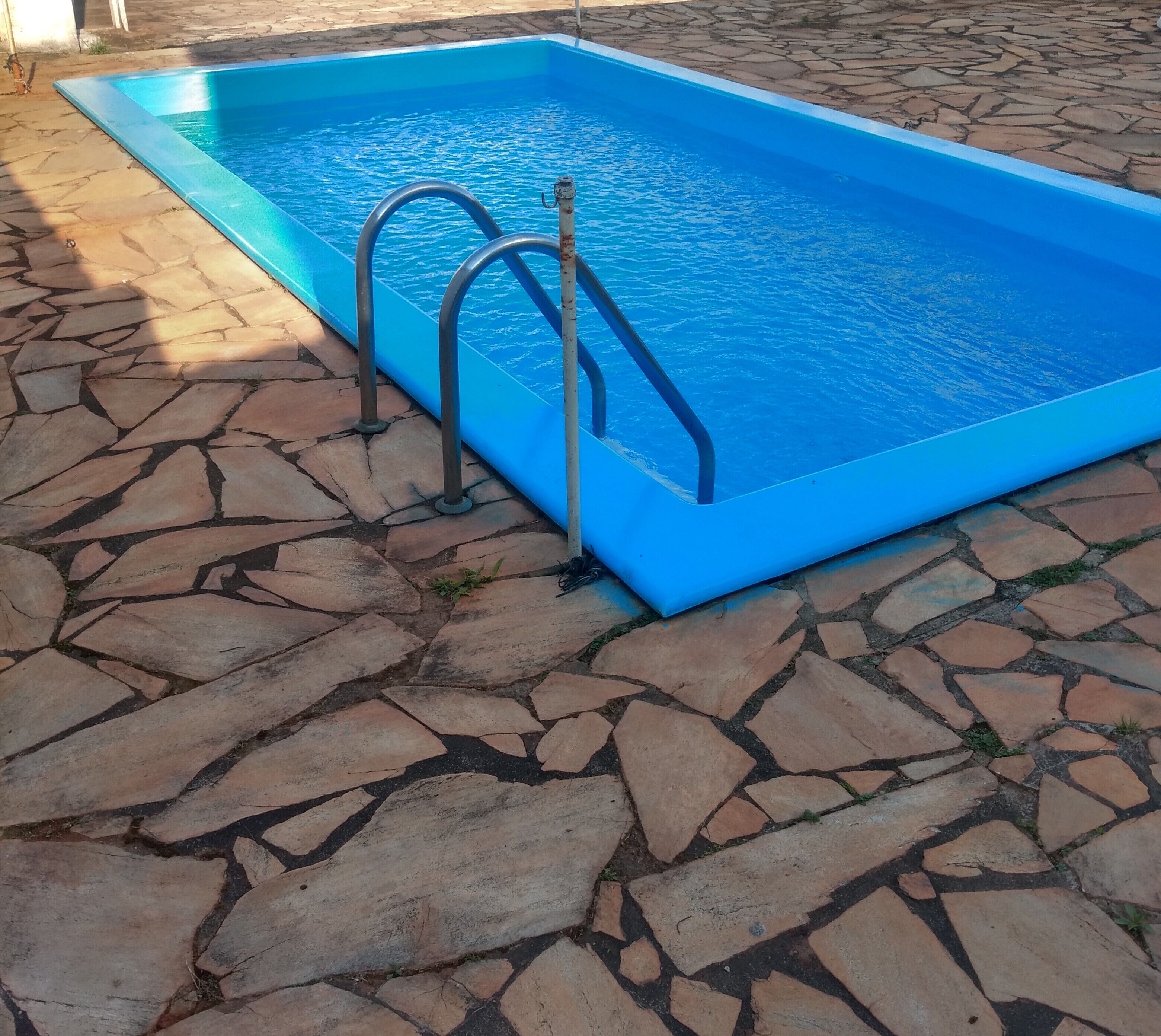 A rectangular swimming pool with a blue interior, surrounded by a stone-tiled deck.