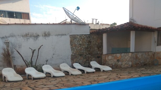 A swimming pool with white lounge chairs and a stone wall. - Pousada Samambaia  (Sao Lourenco)