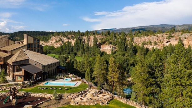 Una cabaña con piscina, mobiliario exterior y vistas a una cadena montañosa boscosa.