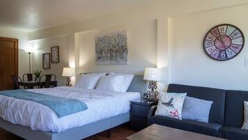 A bedroom with a bed, a sofa, a coffee table, a wall clock, a painting, and a lamp.