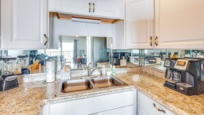 A kitchen with white cabinets, a double sink, a coffee maker, and a blender. - Steps to Shore: PCB Condo w/ Pool Access + Views! (Panama City Beach)