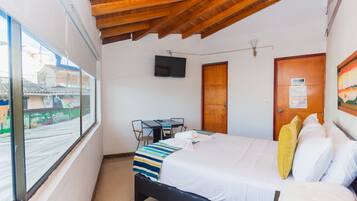 Un dormitorio con cama, televisión, escritorio y ventana.