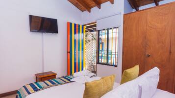 Un dormitorio con cama, televisor montado en la pared, armario de madera y ventana con barrotes.