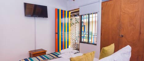 Un dormitorio con cama, televisor montado en la pared, armario de madera y ventana con barrotes.