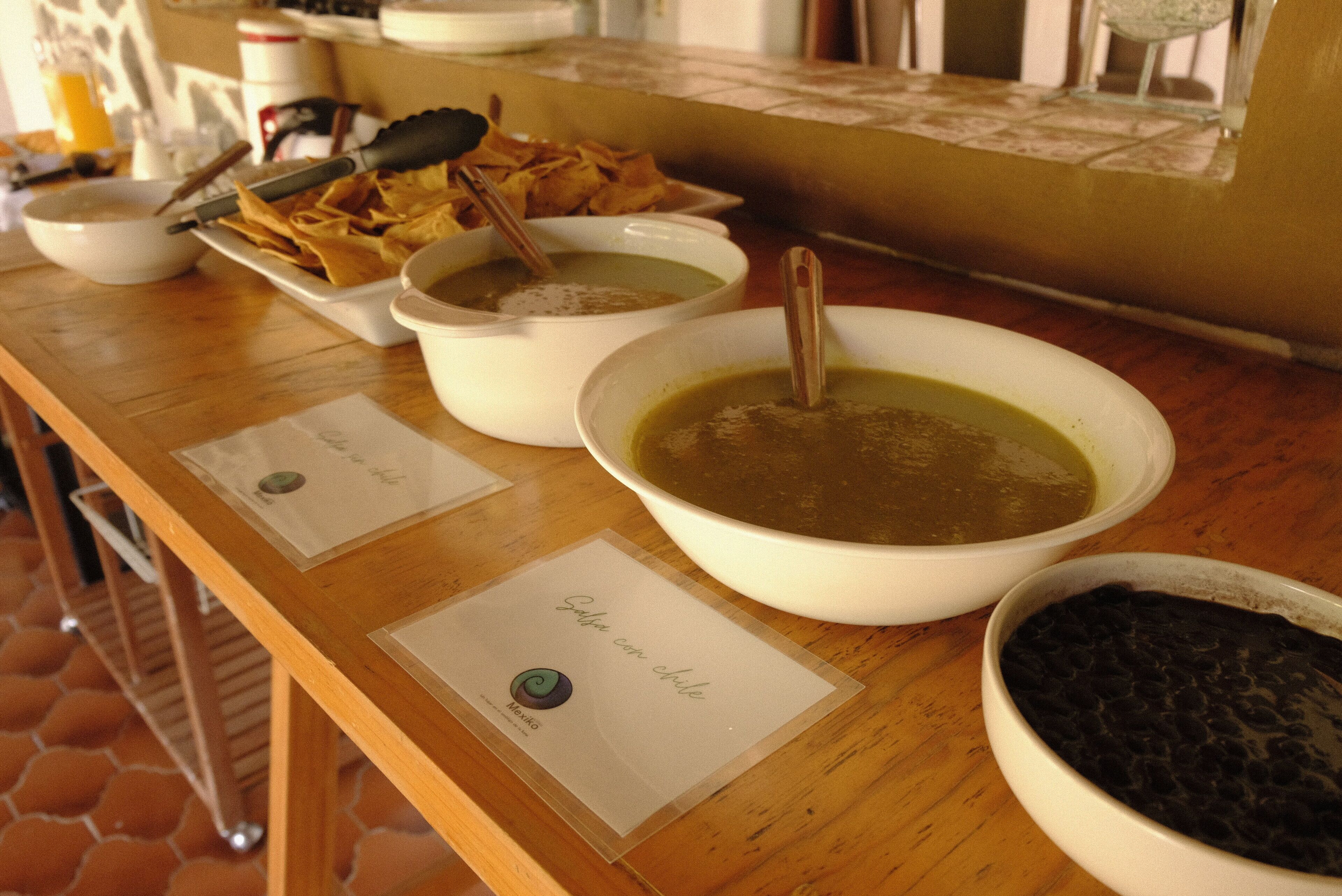 Une table de buffet avec des bols de soupe, des haricots et des chips.