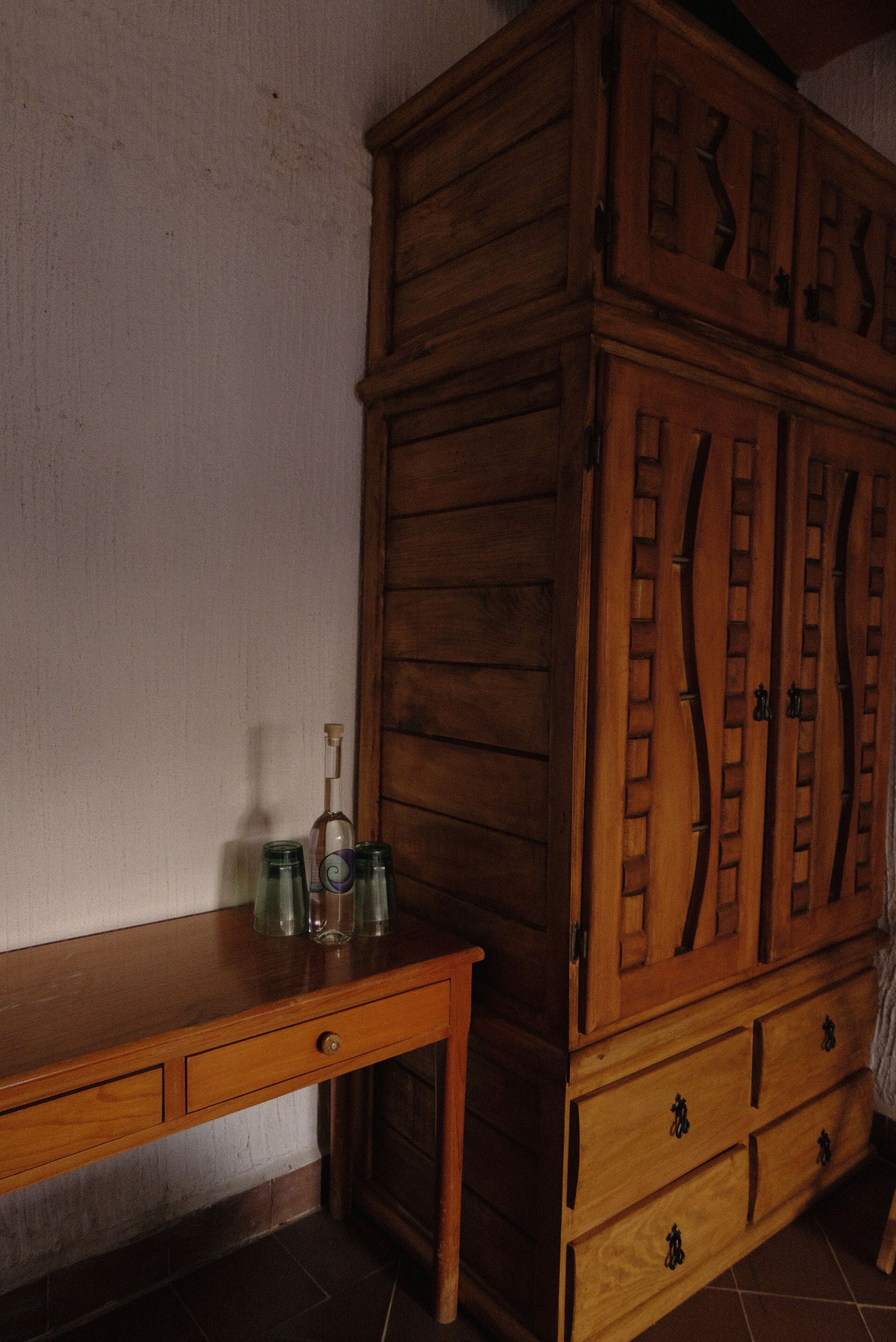 A wooden cabinet with drawers and a wooden table with bottles.