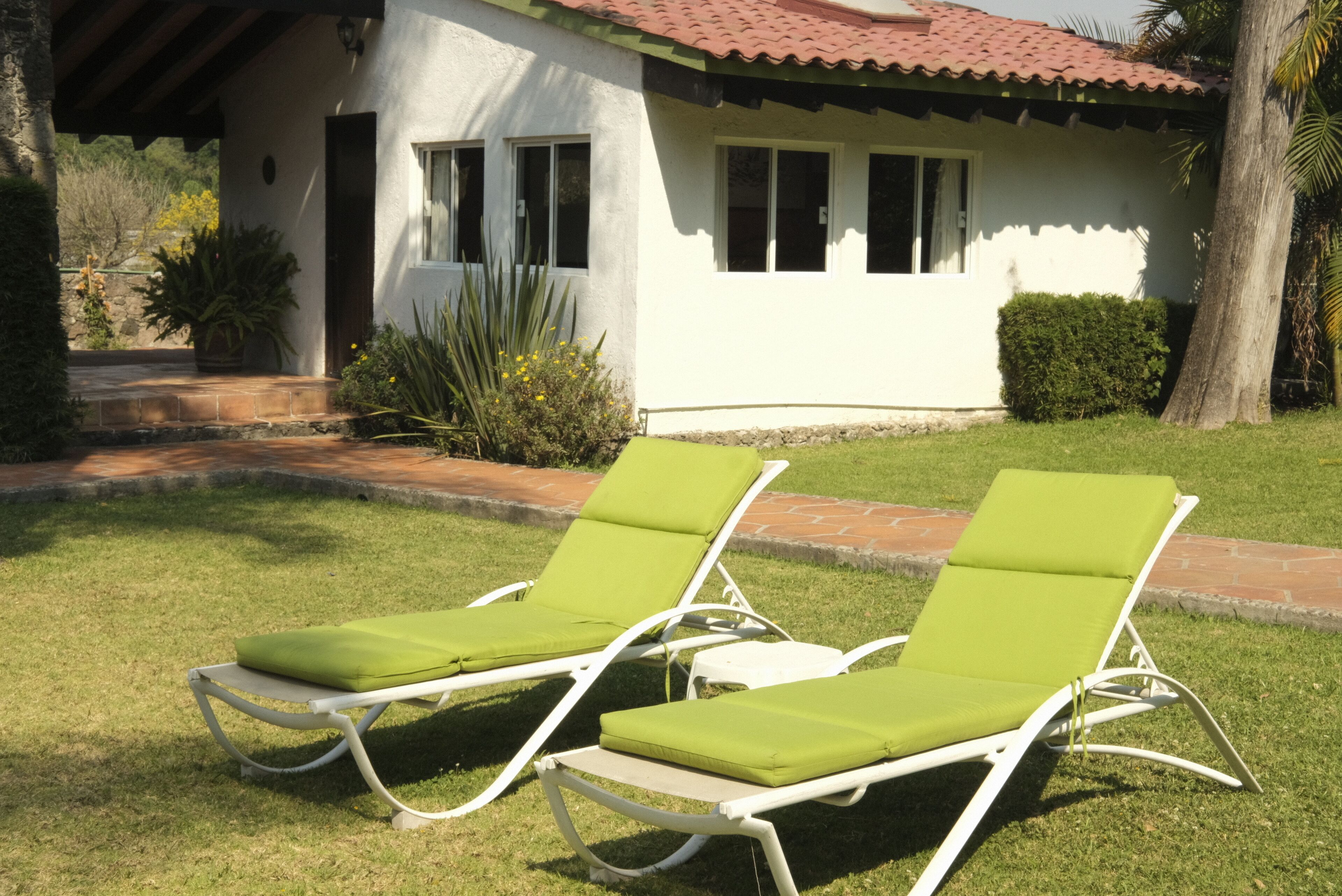 Two green lounge chairs with white frames, a white building with a red-tiled roof, and a well-maintained lawn.