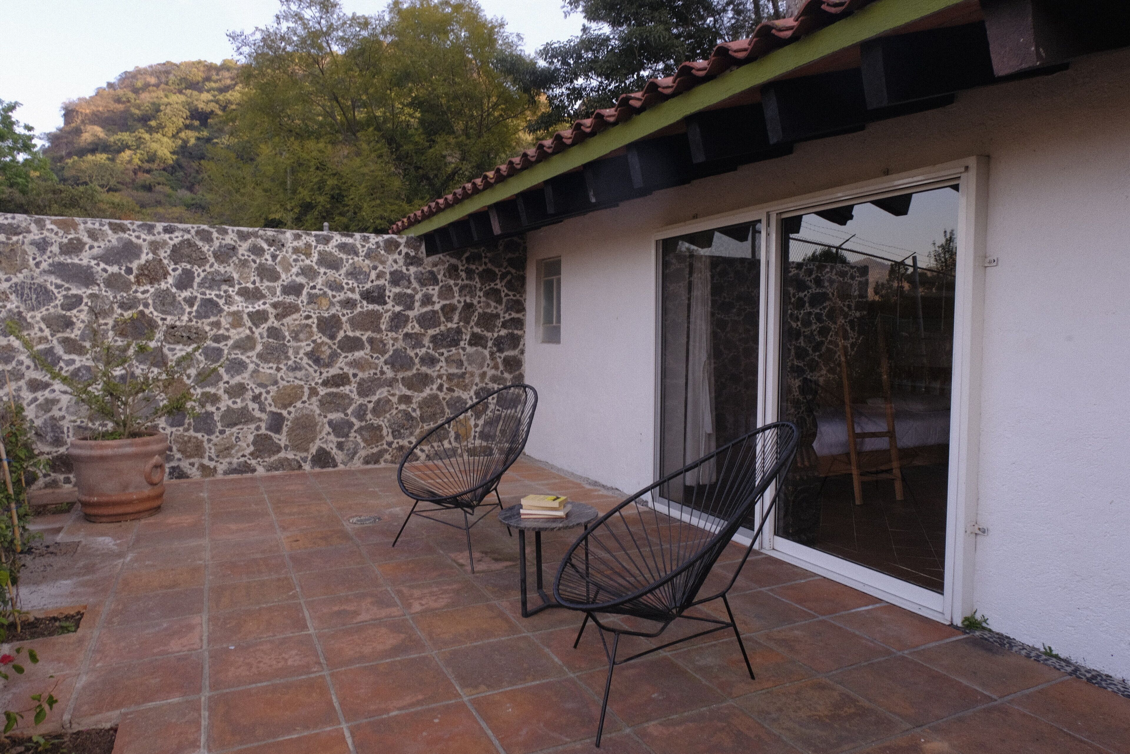 Un patio con paredes de piedra, piso de baldosas y dos sillas de alambre negro.