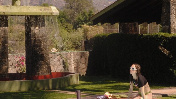 Una persona sentada junto a una piscina, con montañas al fondo.